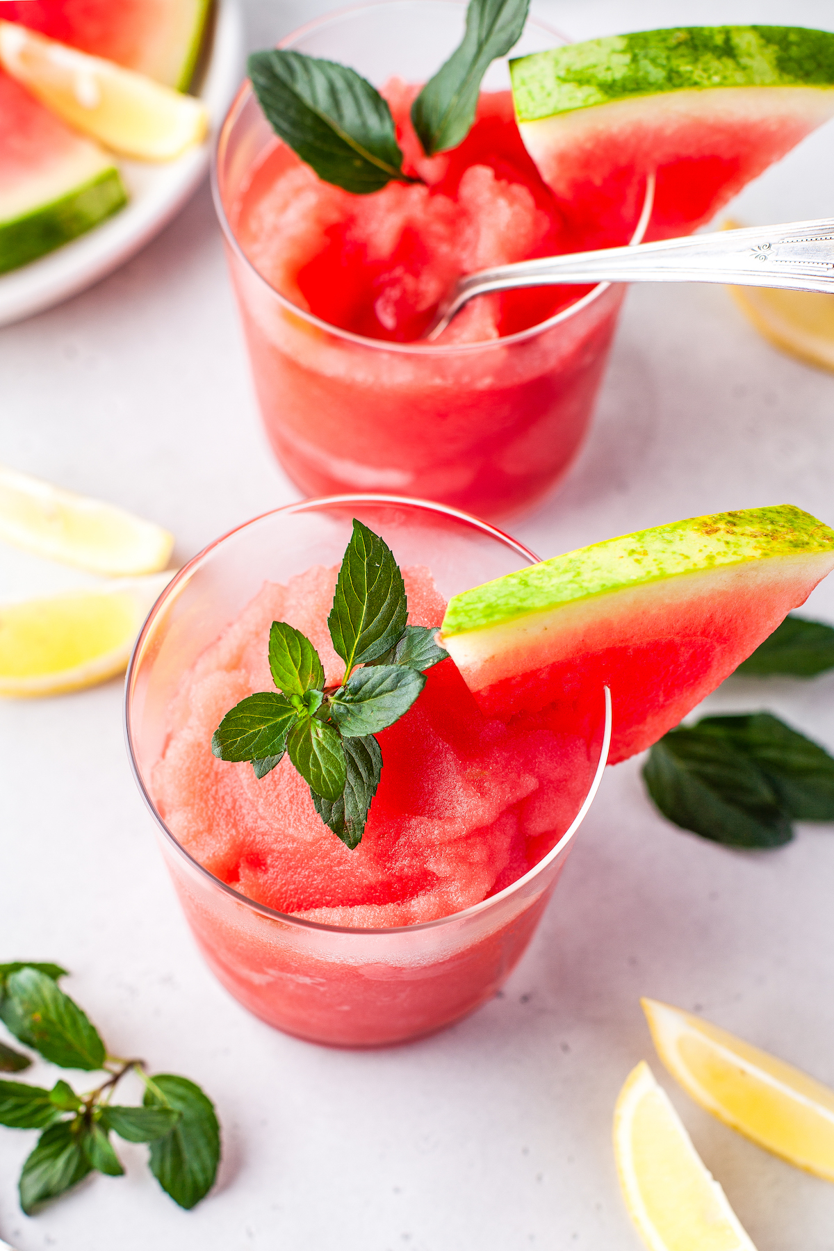 A frozen blended cocktail garnished with a thin watermelon slice, and fresh mint leaves.