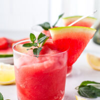 A frozen cocktail garnished with wateremelon and mint.