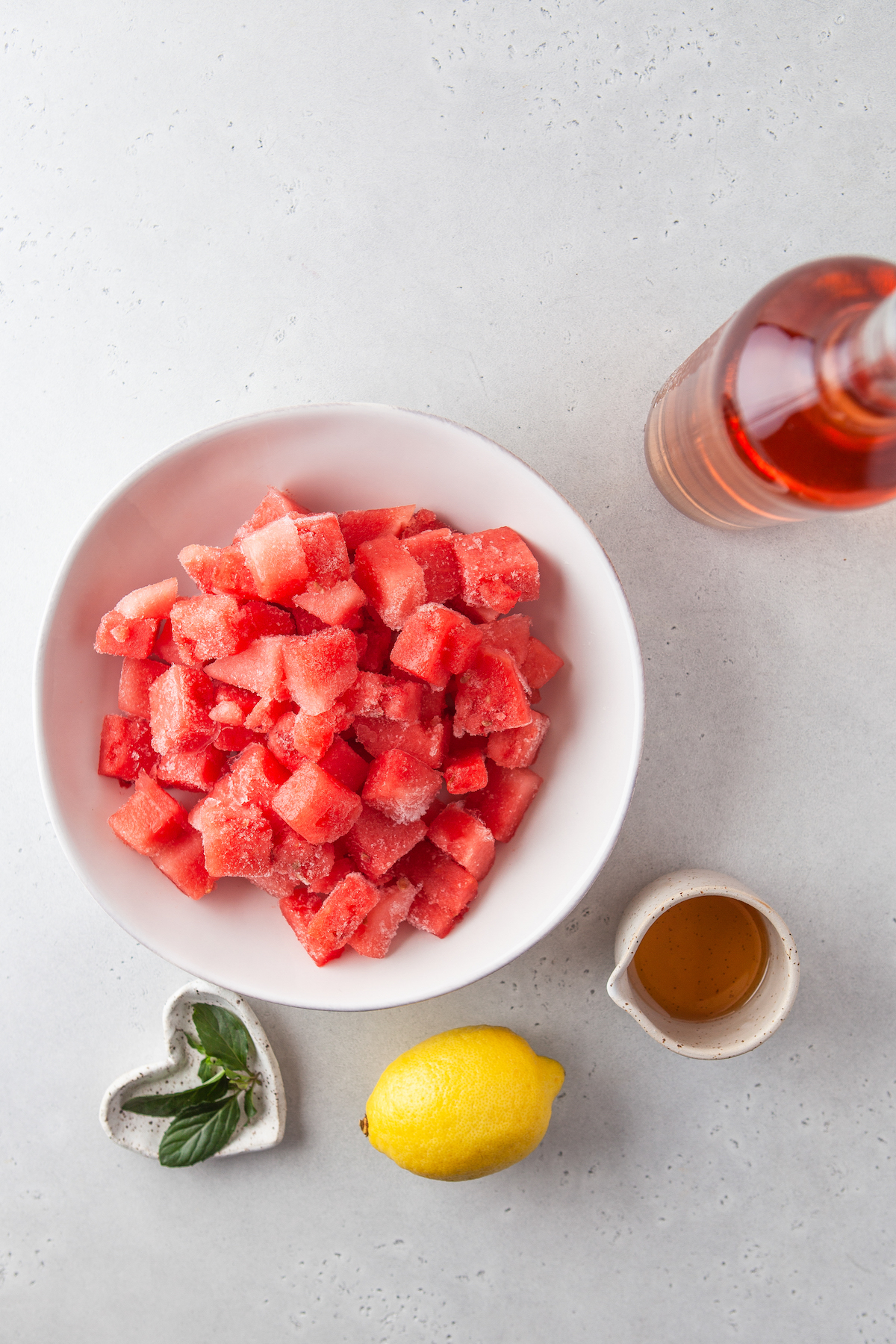 Fresh watermelon chunks, a bottle of wine, a small cup of agave syrup, a lemon, and fresh mint.