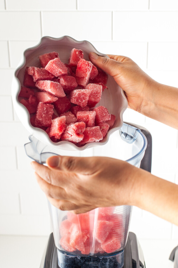 Frozen watermelon chunks being poured into a blender.