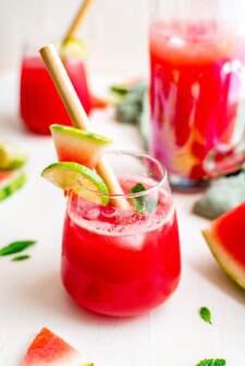 A watermelon margarita in a rocks glass, garnished with lime, watermelon, and a paper straw.