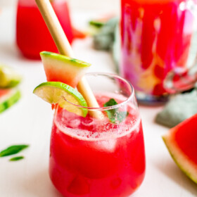 A watermelon margarita in a rocks glass, garnished with lime, watermelon, and a paper straw.