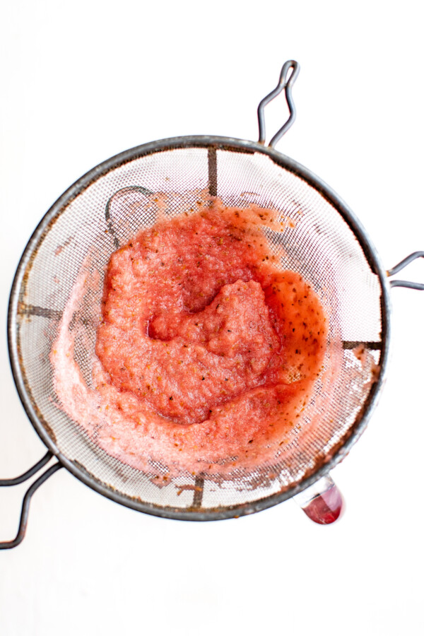 Overhead shot of a strainer full of watermelon pulp, over a pitcher.