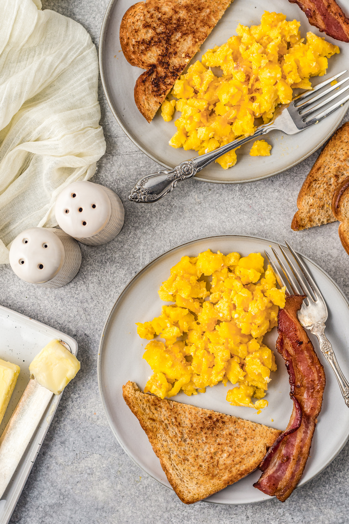 A breakfast spread of air fryer scrambled eggs on plates, next to toast and bacon.