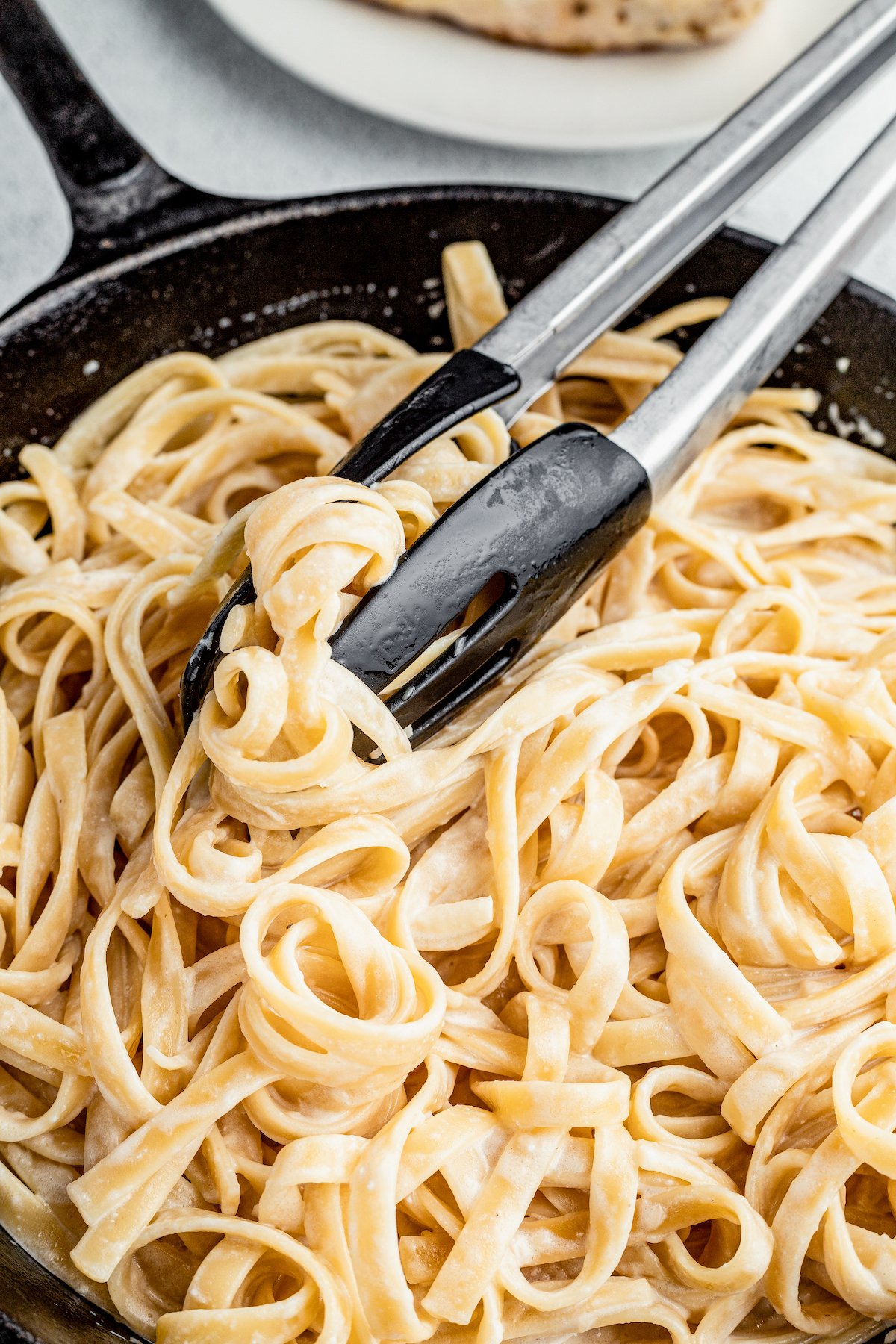 Pasta being tossed with tongs to mix in the cream sauce.