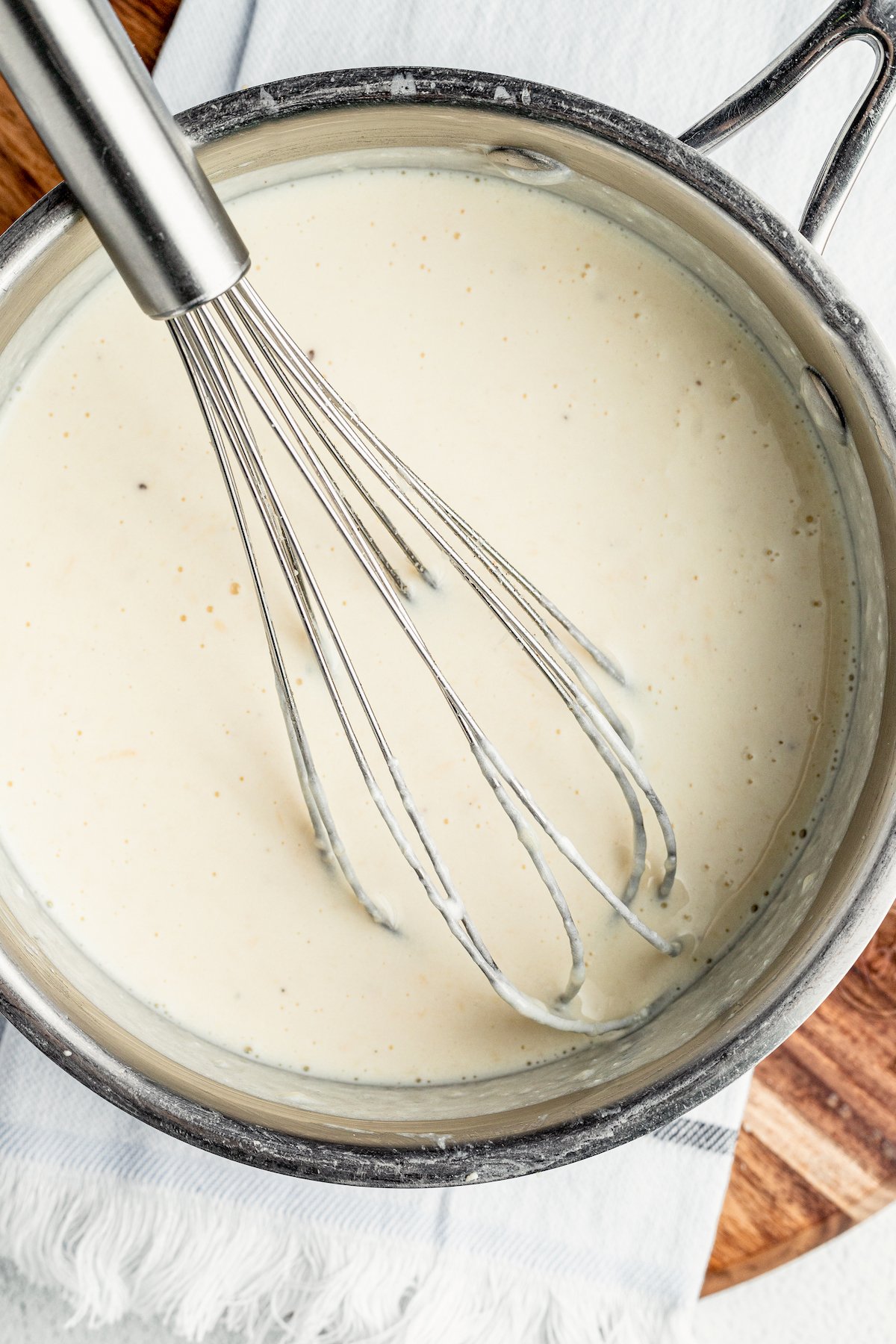 A creamy sauce being whisked in a saucepan.