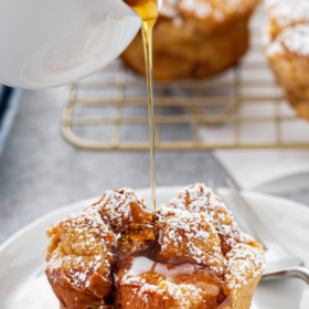 Maple syrup being poured on top of a muffin on a plate.