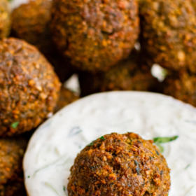 Falafel being dunked in tzatziki in a bowl.