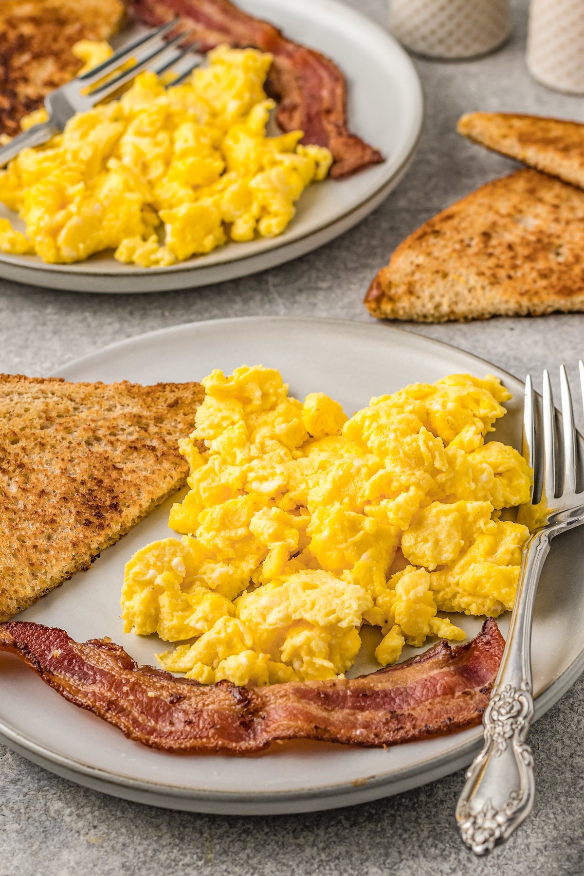 Two plates of Instant Pot scrambled eggs with slices of toast and bacon.