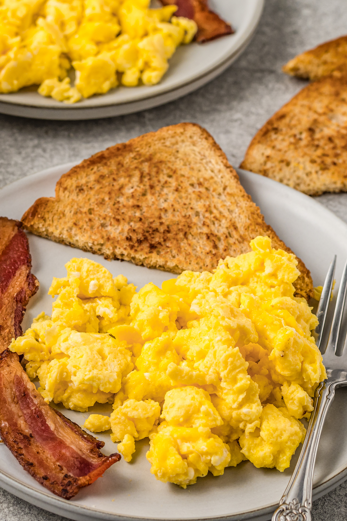Scrambled eggs on a plate next to toast and bacon.