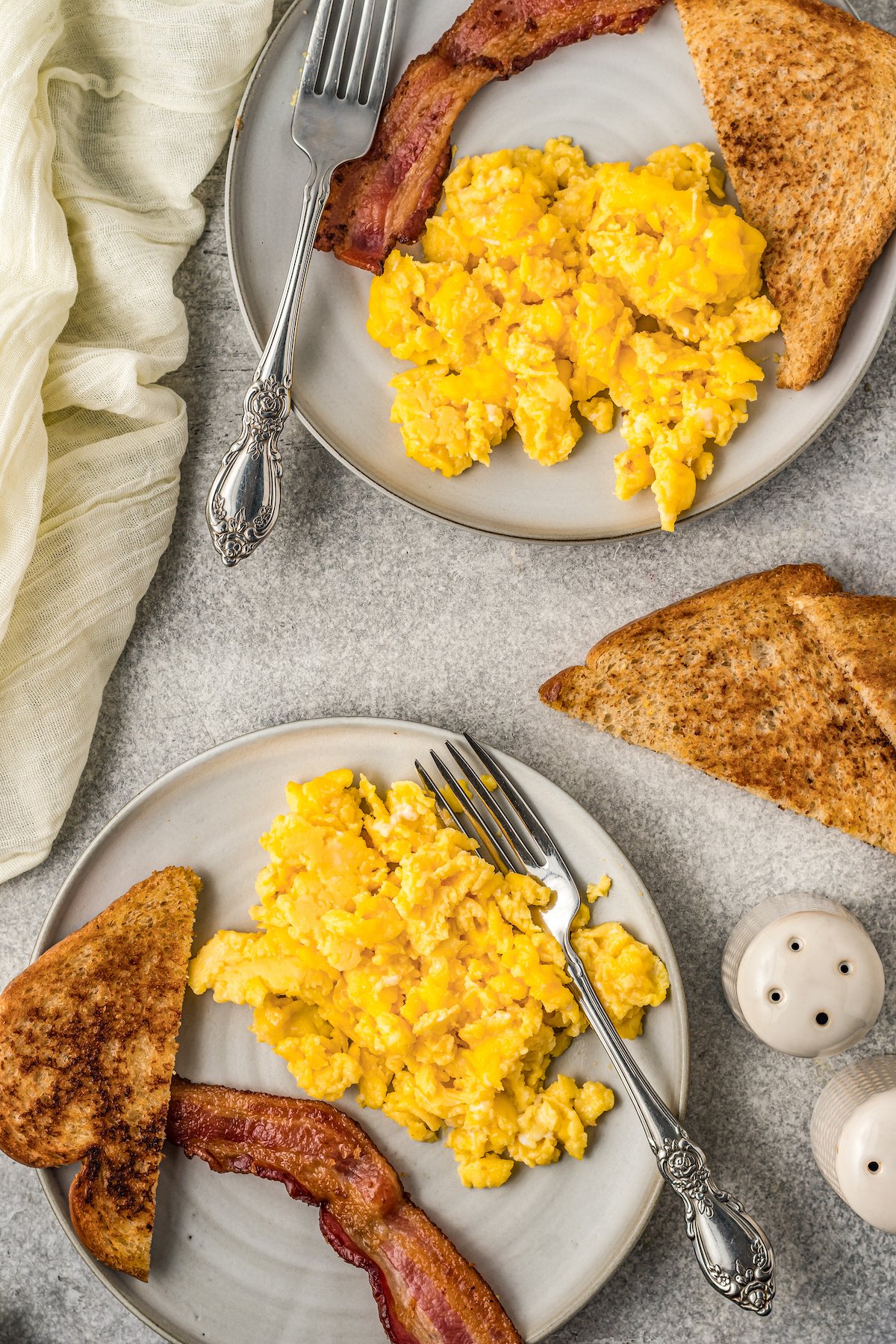 Two plates of Instant Pot scrambled eggs with slices of toast and bacon.