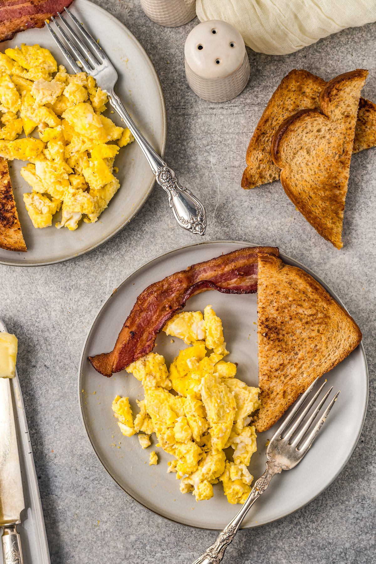 A breakfast spread of scrambled eggs on plates, next to toast and bacon.