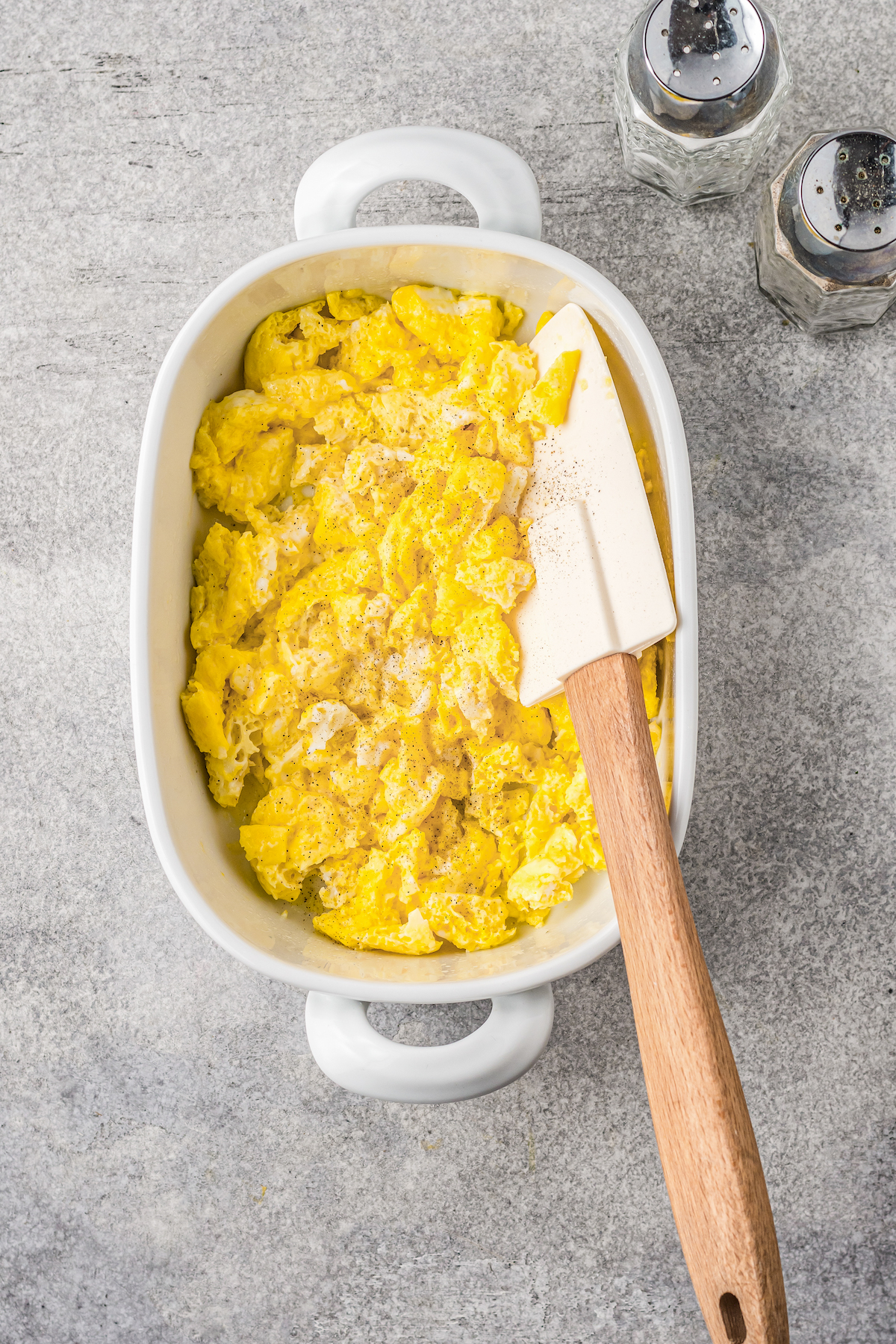 Scrambled eggs in a white microwave-safe dish next to a spatula.