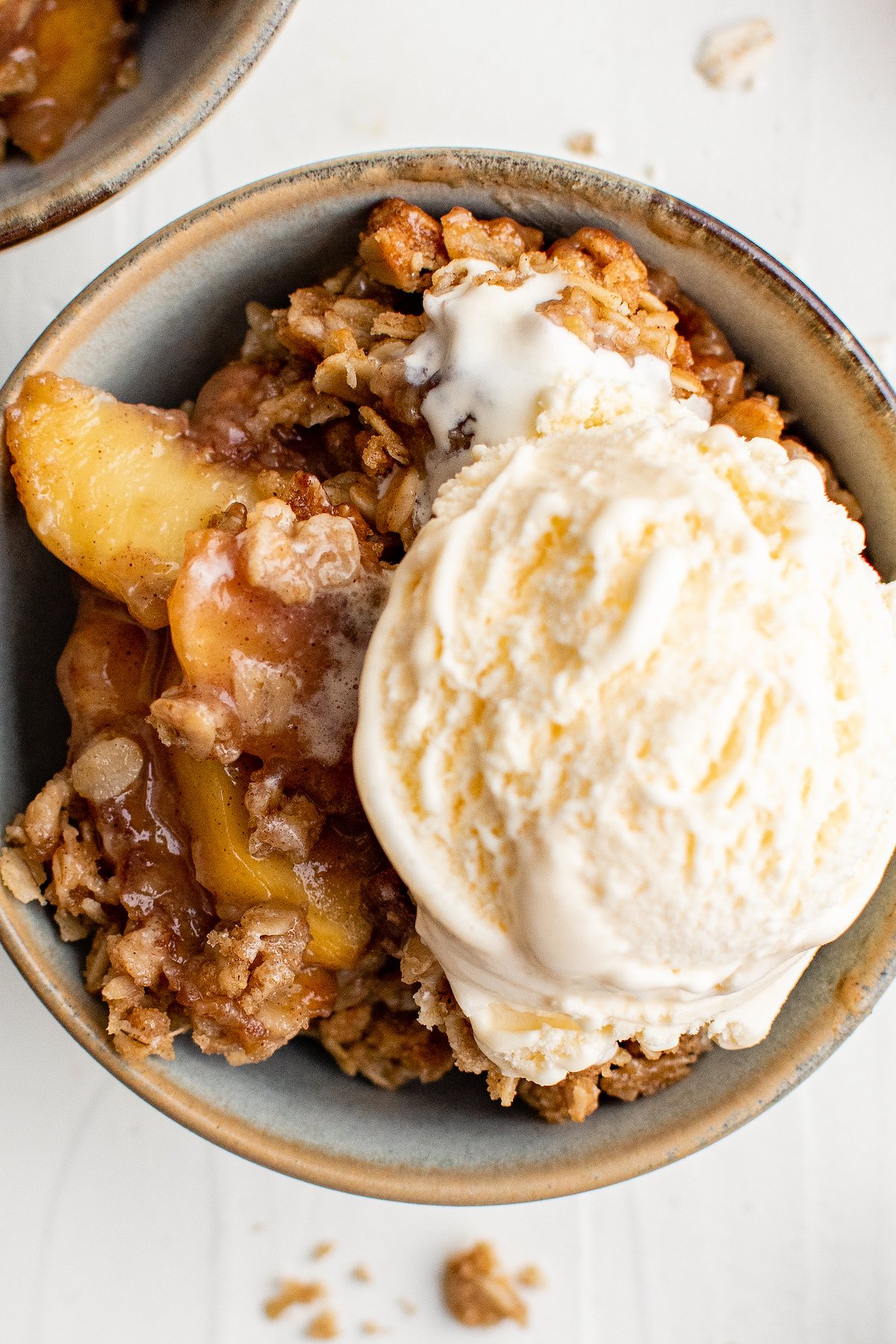 A bowl of peach dessert with vanilla ice cream on top.