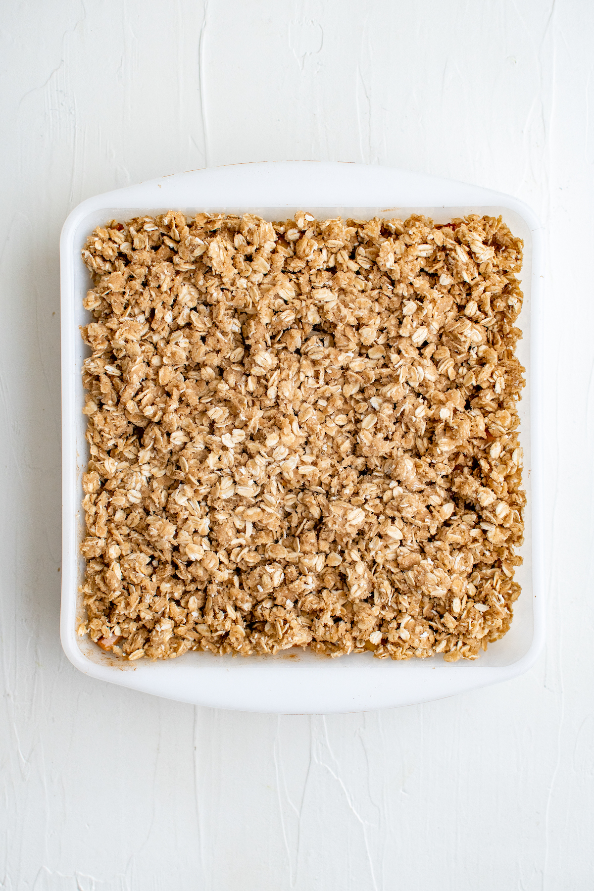 An unbaked peach crisp in a square baking dish.