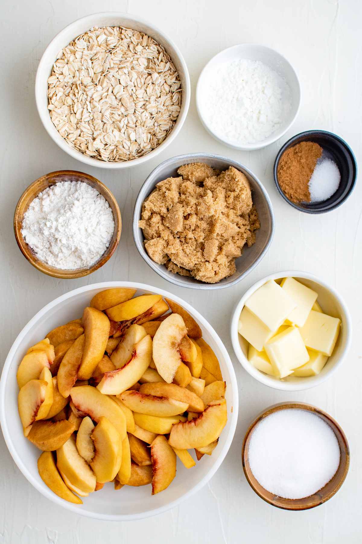 From top left: Rolled oats, cornstarch, flour, brown sugar, spices, peeled and sliced peaches, butter, granulated sugar.