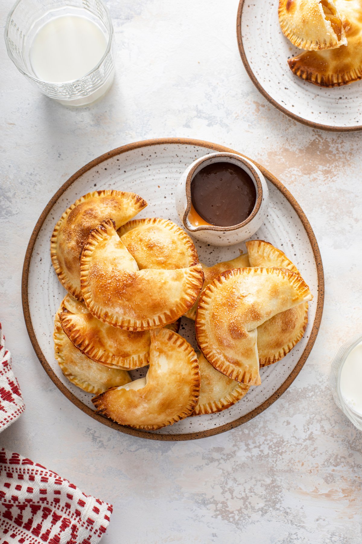 Overhead shot of a platter of empanadas on a platter, with a small syrup pitcher filled with caramel sauce.