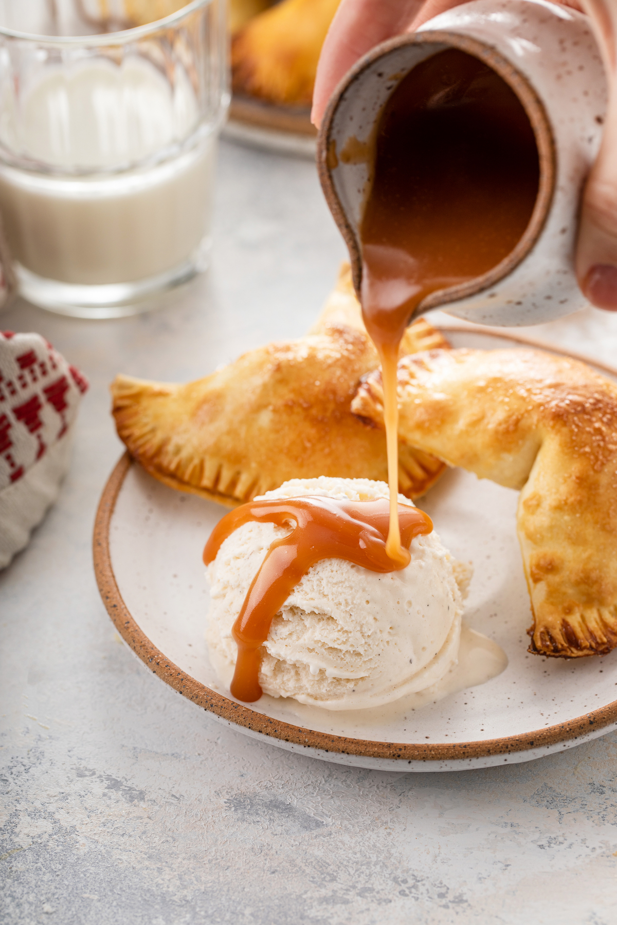 Two hand pies on a plate with a scoop of ice cream. Caramel sauce is being drizzled over the ice cream.