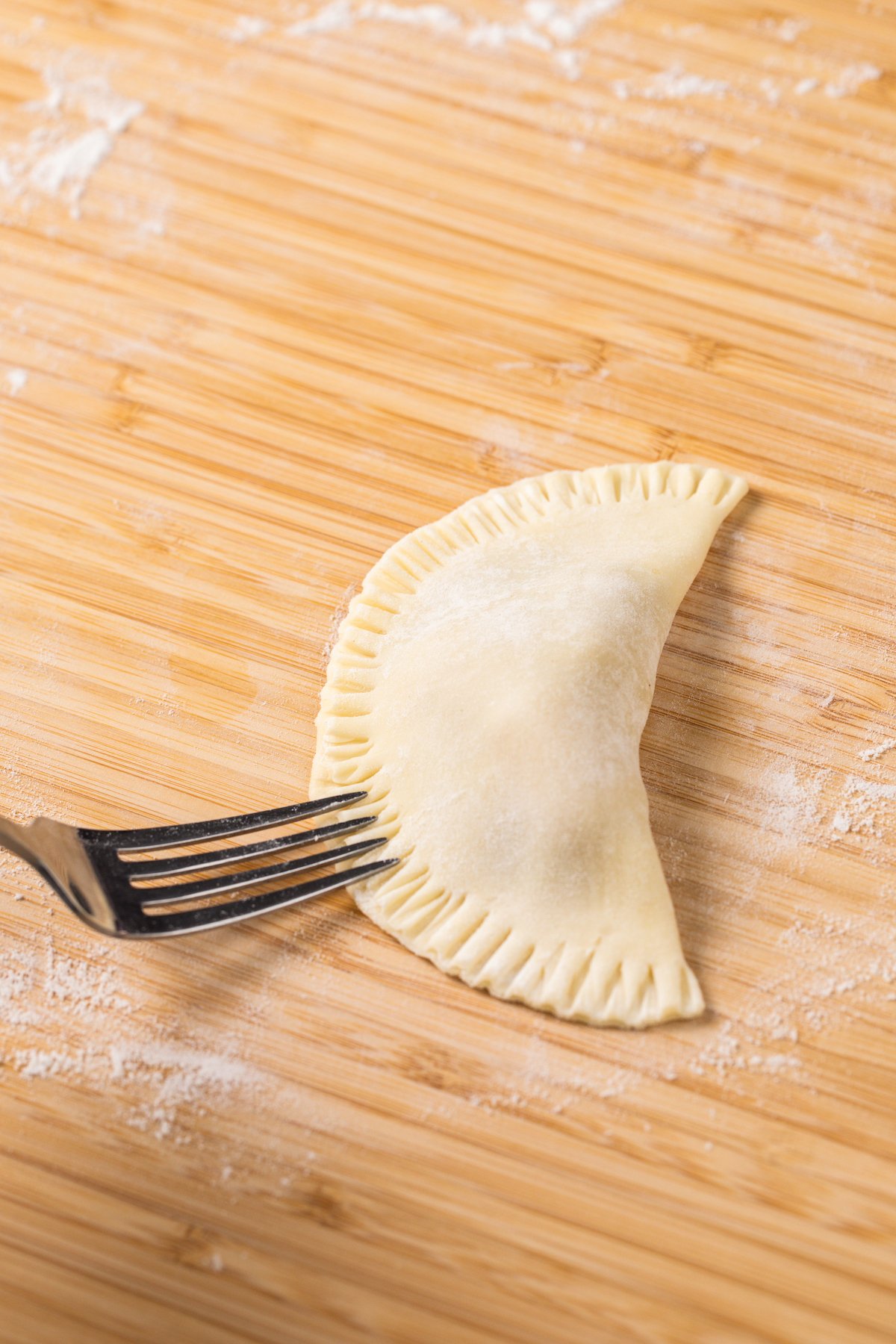 A fork pressing down on the edges of an unbaked empanada, crimping the border.