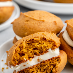 Pumpkin whoopie pies on a white plate with a bite taken out of one.