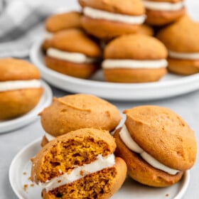 Pumpkin whoopie pies on a white plate with a bite taken out of one whoopie pie.