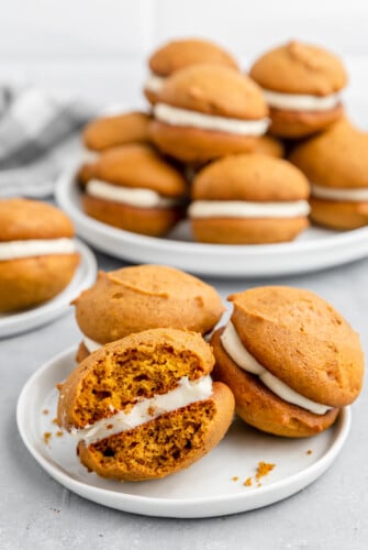 Pumpkin whoopie pies on a white plate with a bite taken out of one whoopie pie.