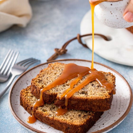 Slices of sweet quick bread on a small plate, with caramel sauce being drizzled over the top.