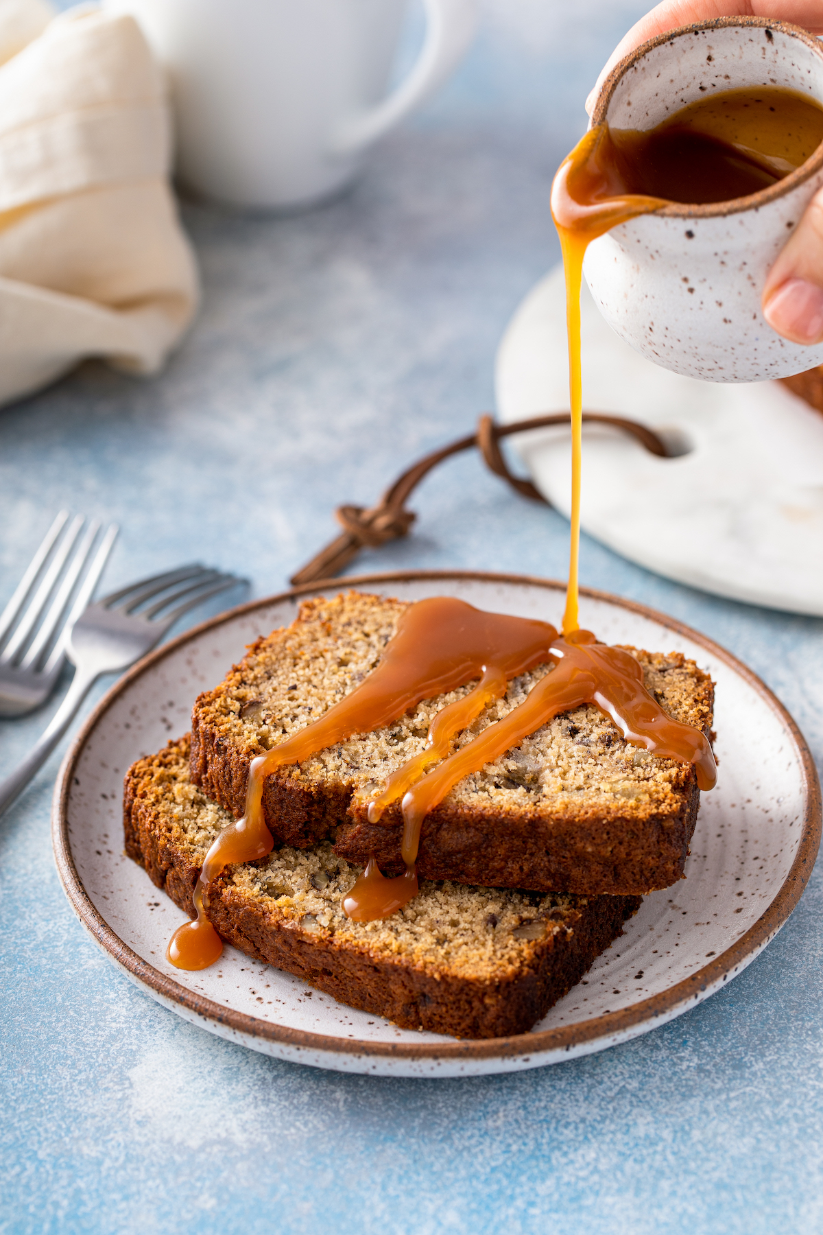 Slices of sweet quick bread on a small plate, with caramel sauce being drizzled over the top.