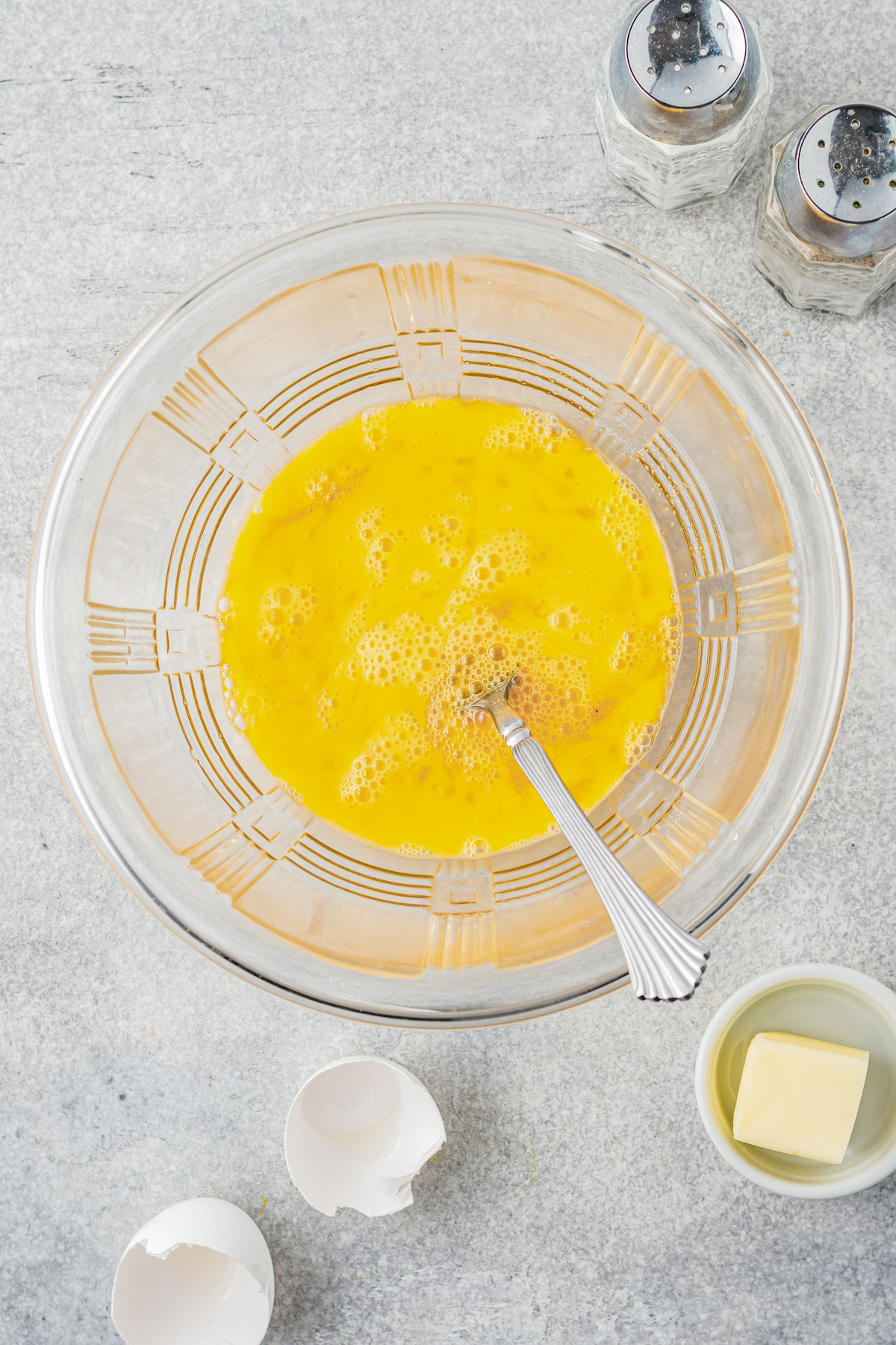 Whisked eggs in a clear mixing bowl with a fork.