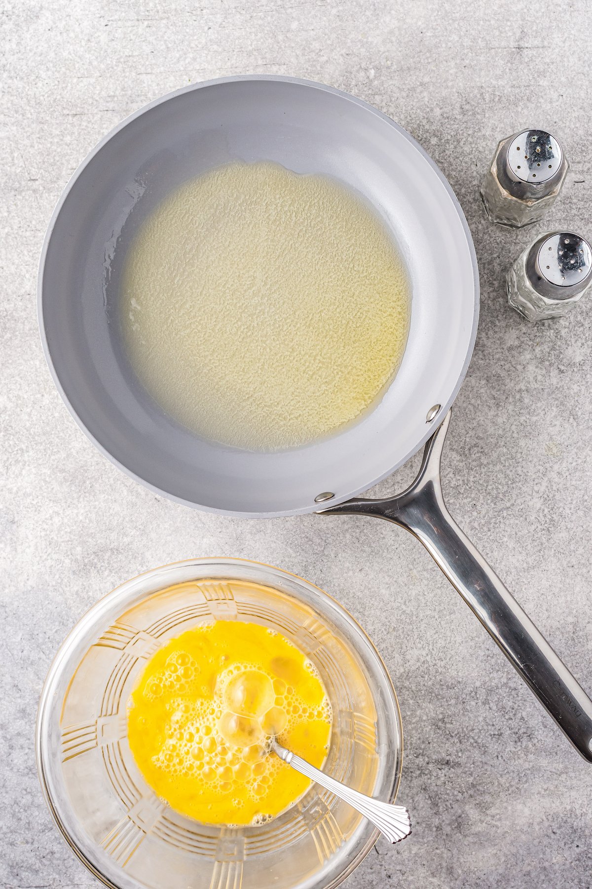 A bowl of whisked eggs next to a skillet with melted butter.