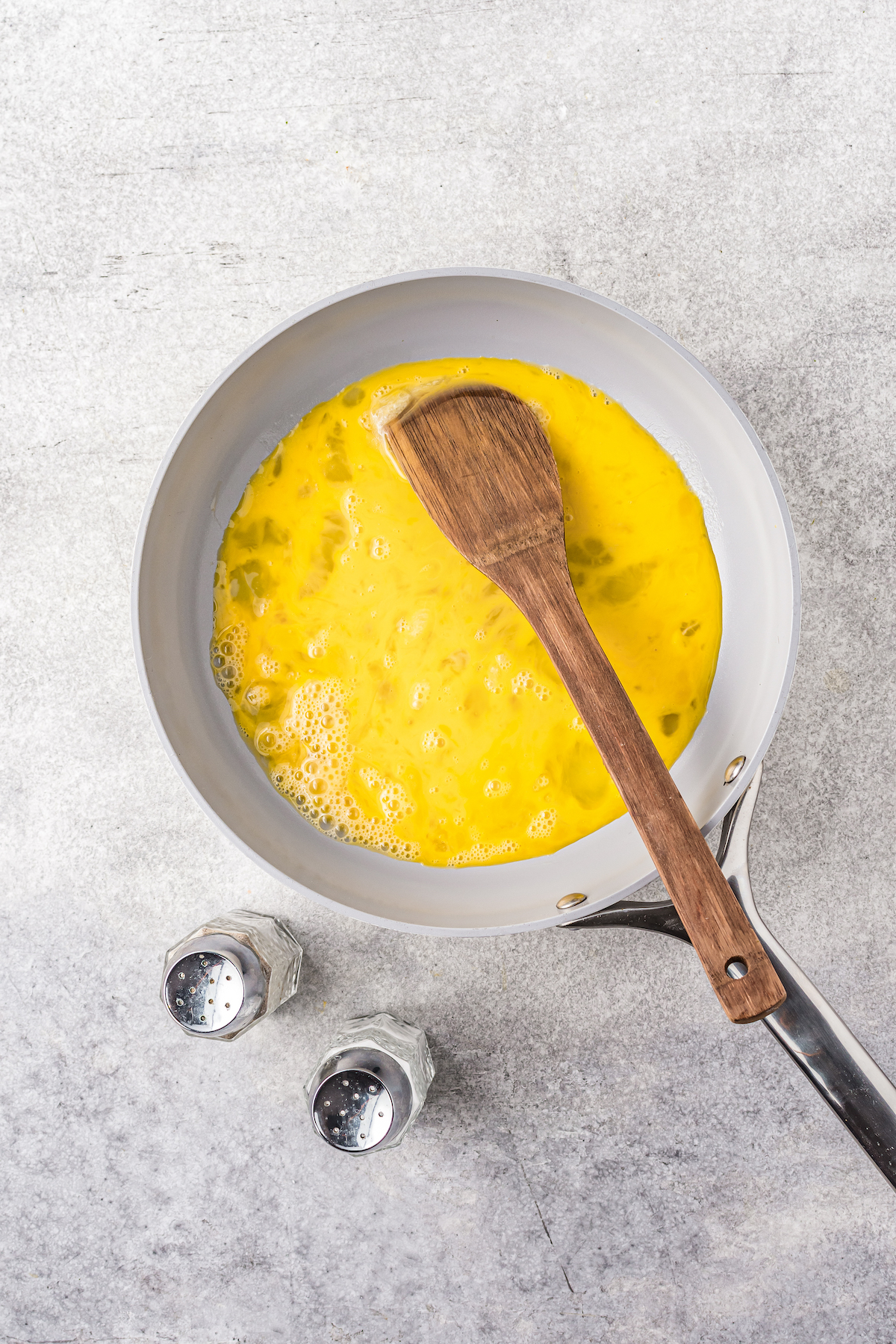 A wooden spatula is used to scramble eggs in a skillet as they cook.
