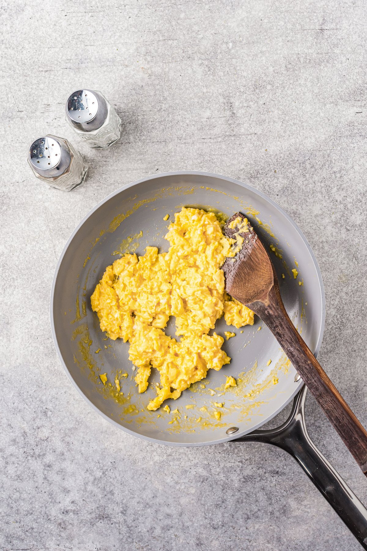 A wooden spatula is used to scramble eggs in a skillet as they cook.