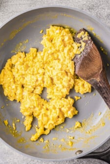 Close up of scrambled eggs in a skillet next to a wooden spatula.