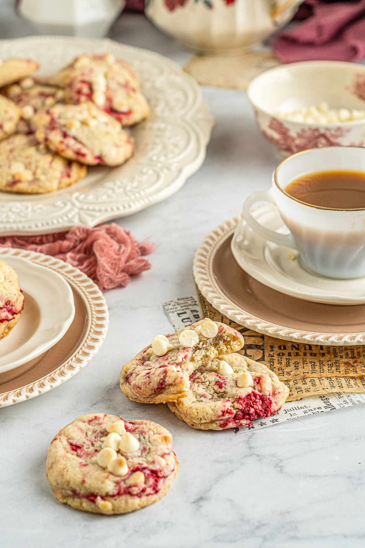 Cookies on a platter next to a cup of tea. Additional cookies are arranged artistically on the table and on dessert plates.