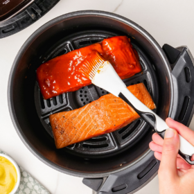 Salmon in an air fryer being brushed with sauce.
