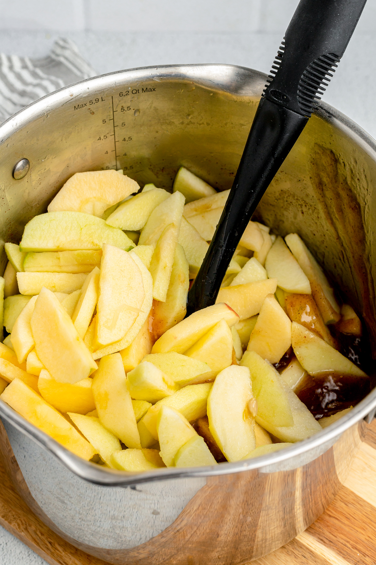 Apple slices are added into a large metal pot with simmering sauce.