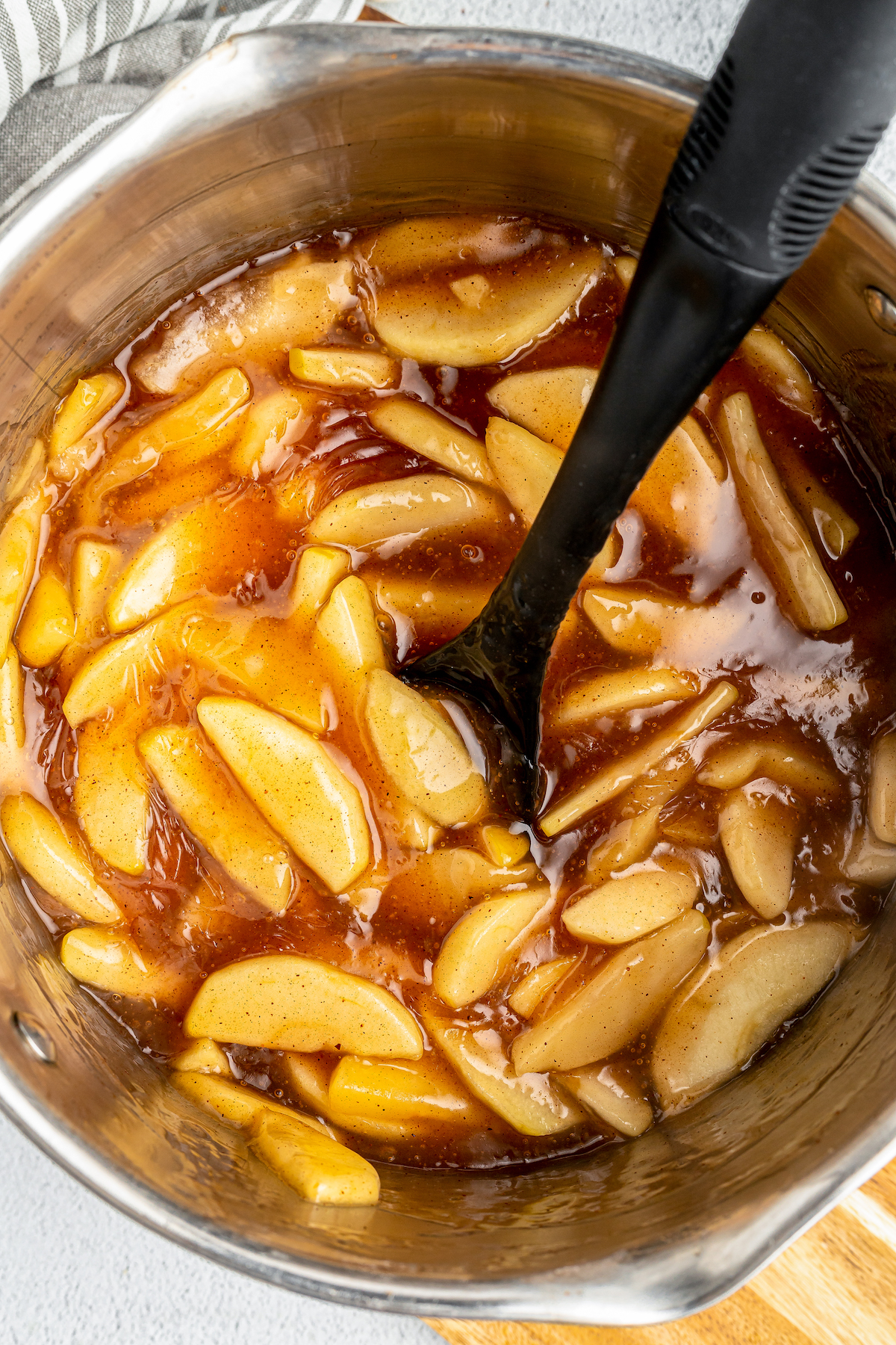 Apple slices in a large metal pot with simmering sauce.