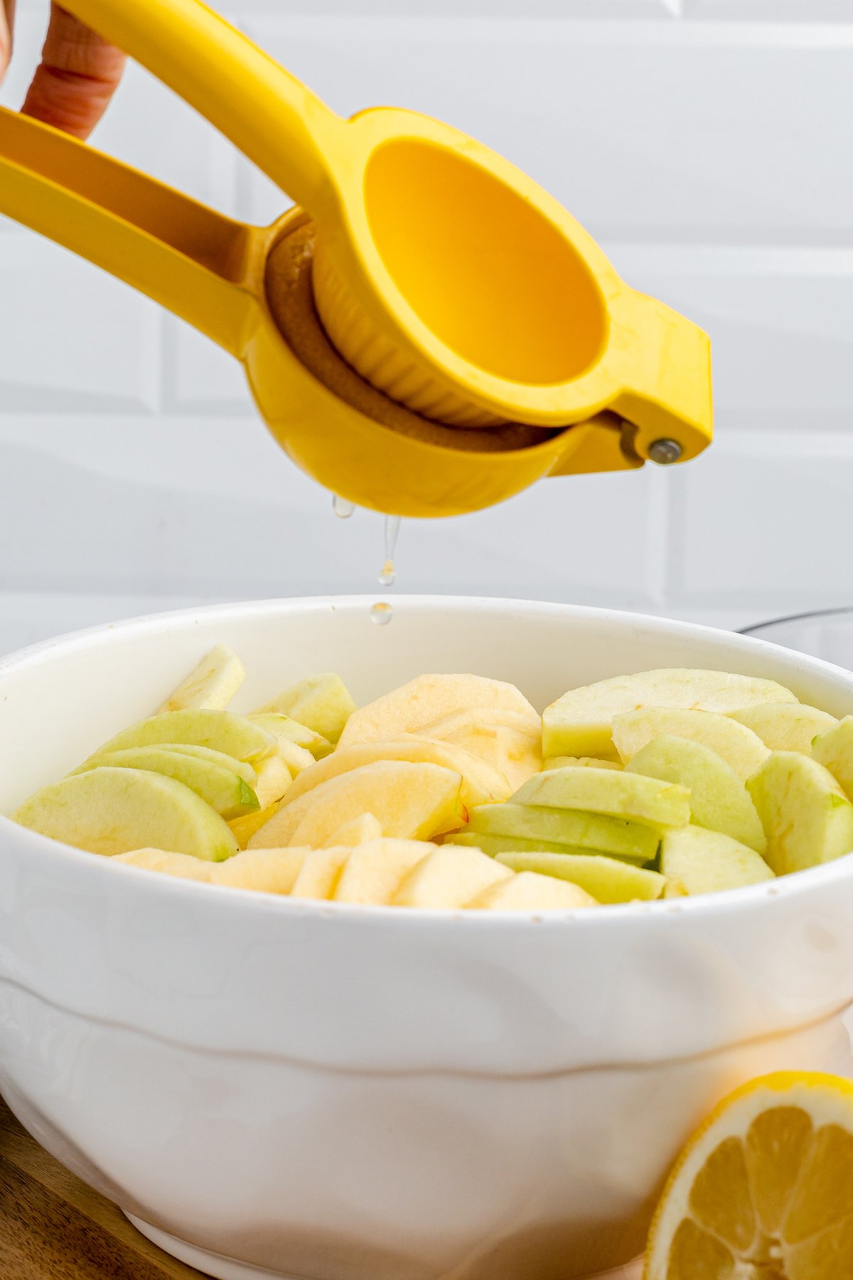 A lemon is squeezed overtop a bowl of apple slices.