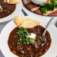 Black bean soup served in bowls topped with sour cream, cilantro, green onions and tortilla chips.