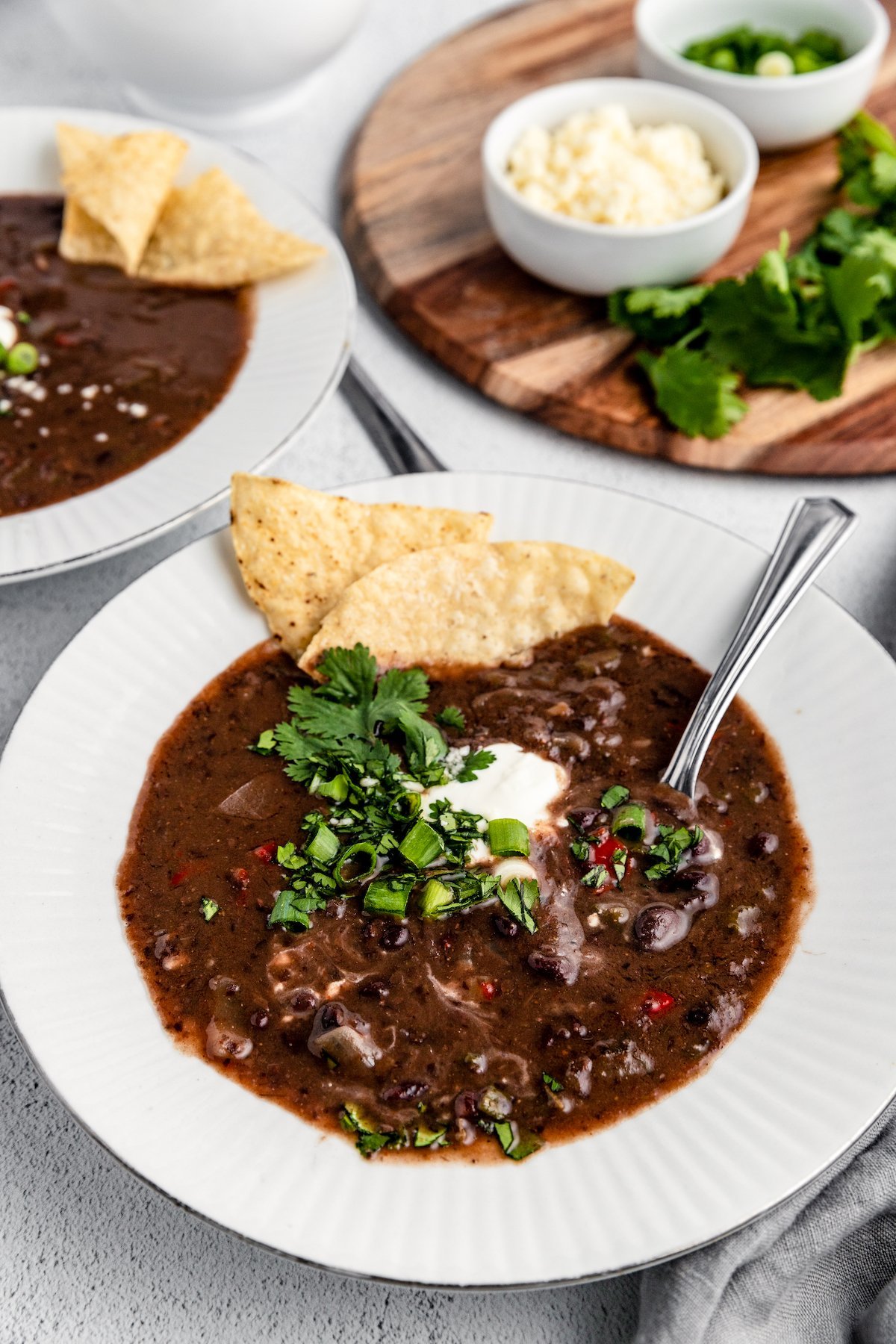 Black bean soup served in bowls topped with sour cream, cilantro, green onions and tortilla chips.