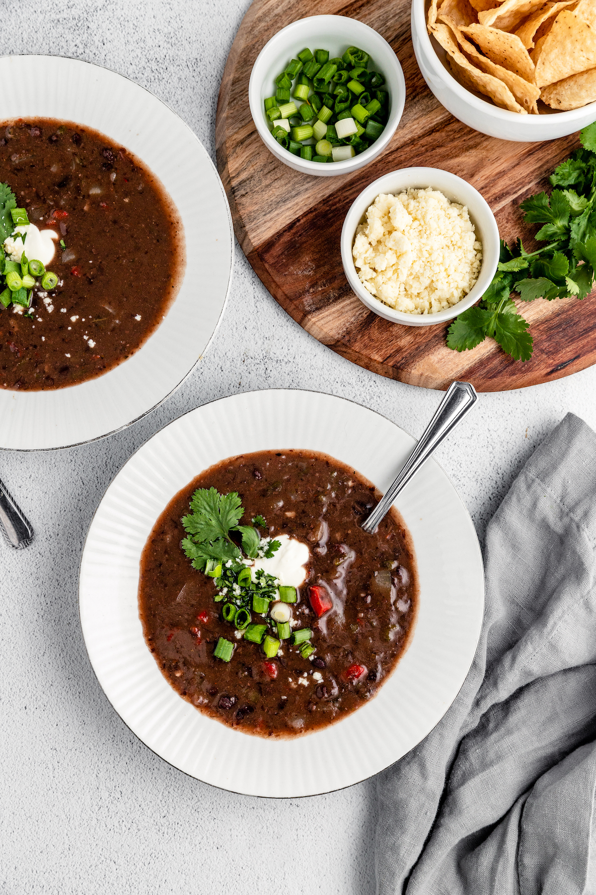 Two bowls of black bean soup garnished with cilantro and sour cream, next to a tray of toppings.