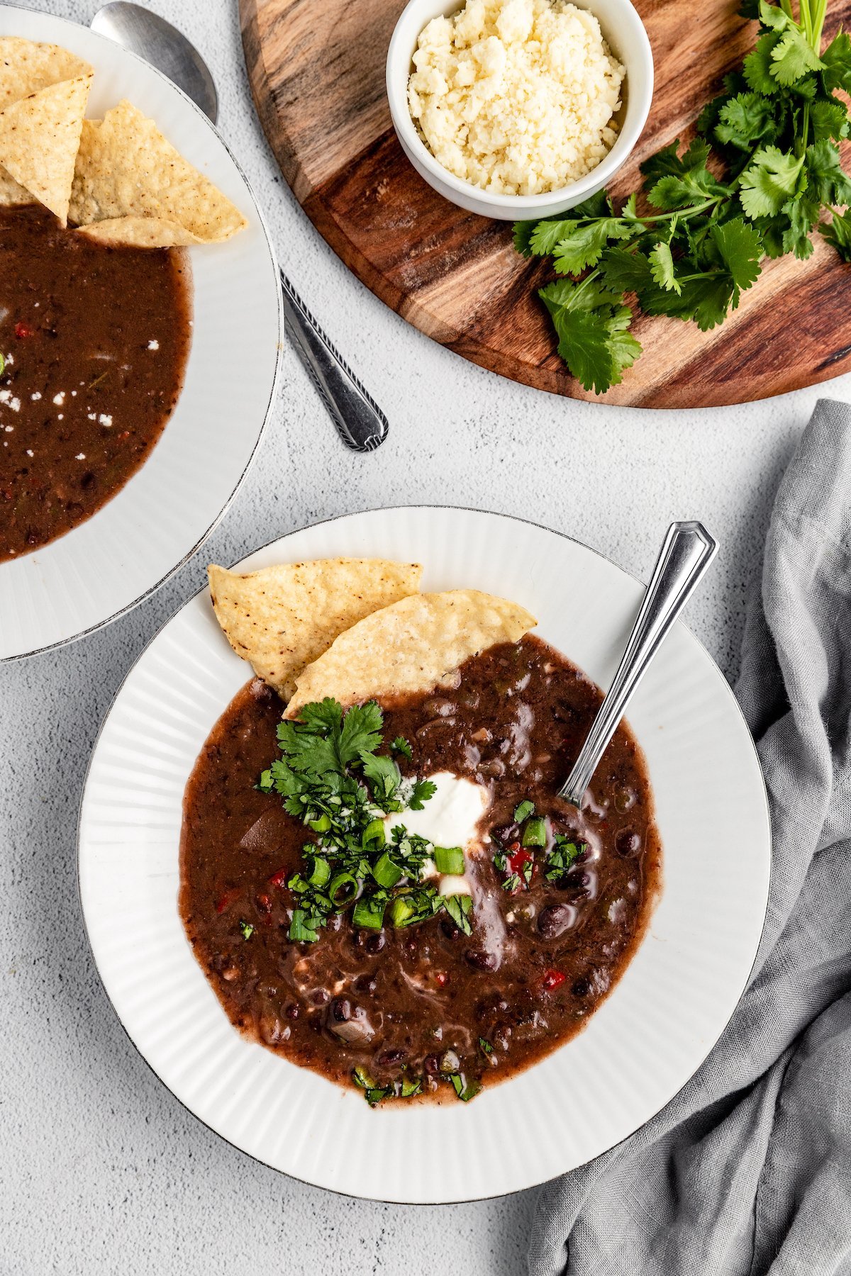 Black bean soup served in bowls topped with sour cream, cilantro, green onions and tortilla chips.