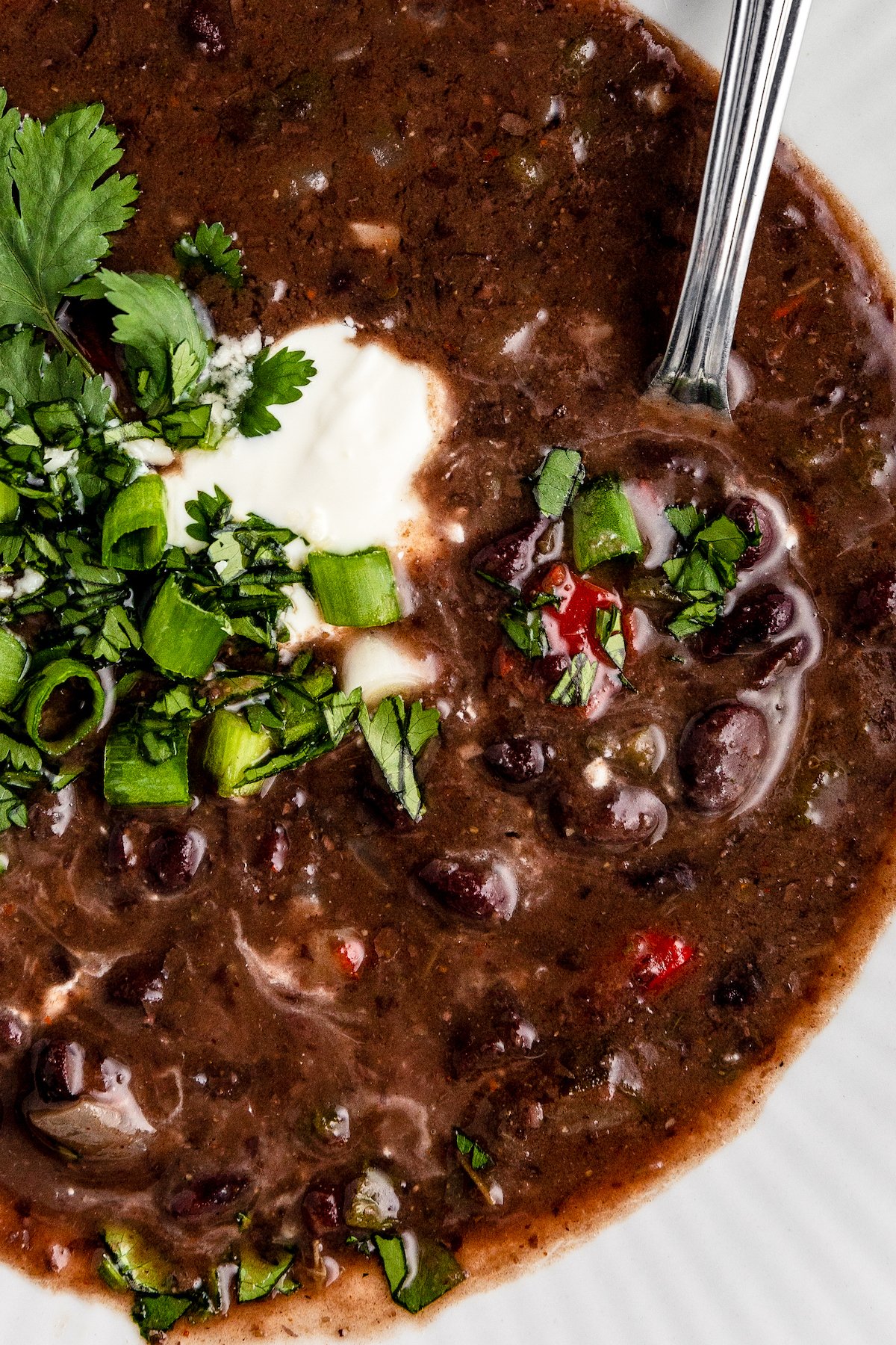 Close up of black bean soup in a bowl with a spoon, topped with sour cream and cilantro.