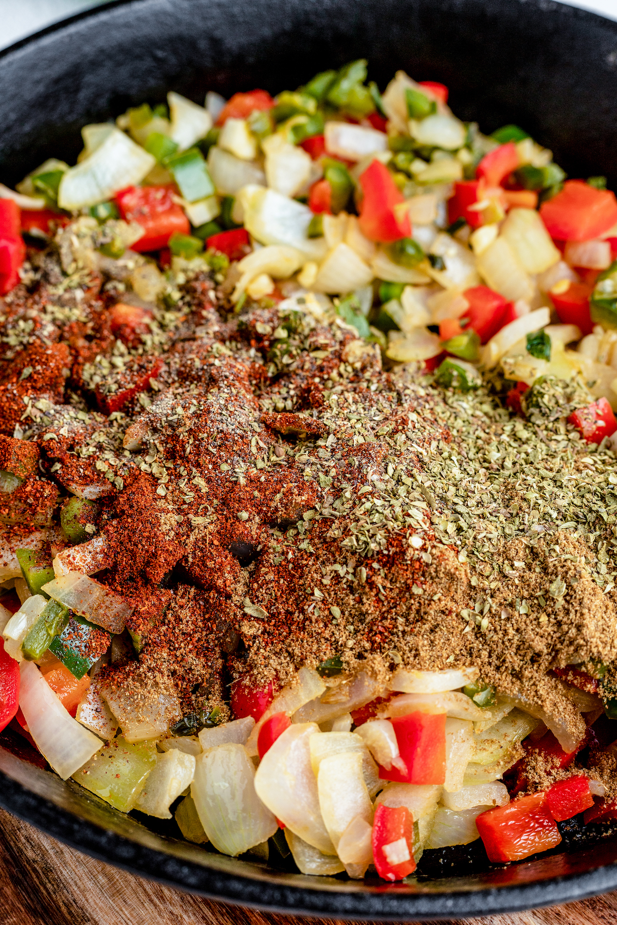 Spices are added into a skillet with sautéed vegetables.