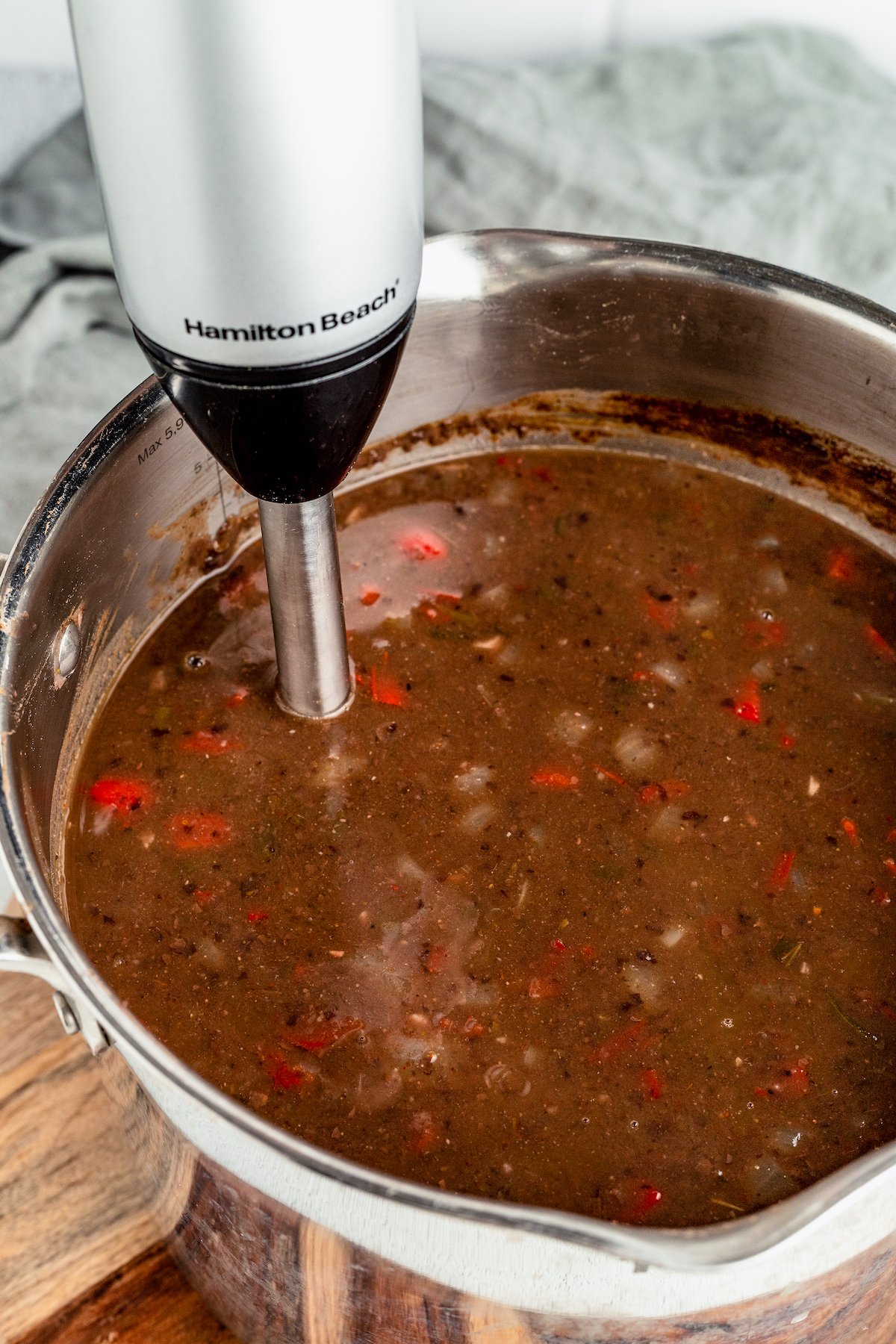 An immersion blender is used to thicken black bean soup inside a large pot.