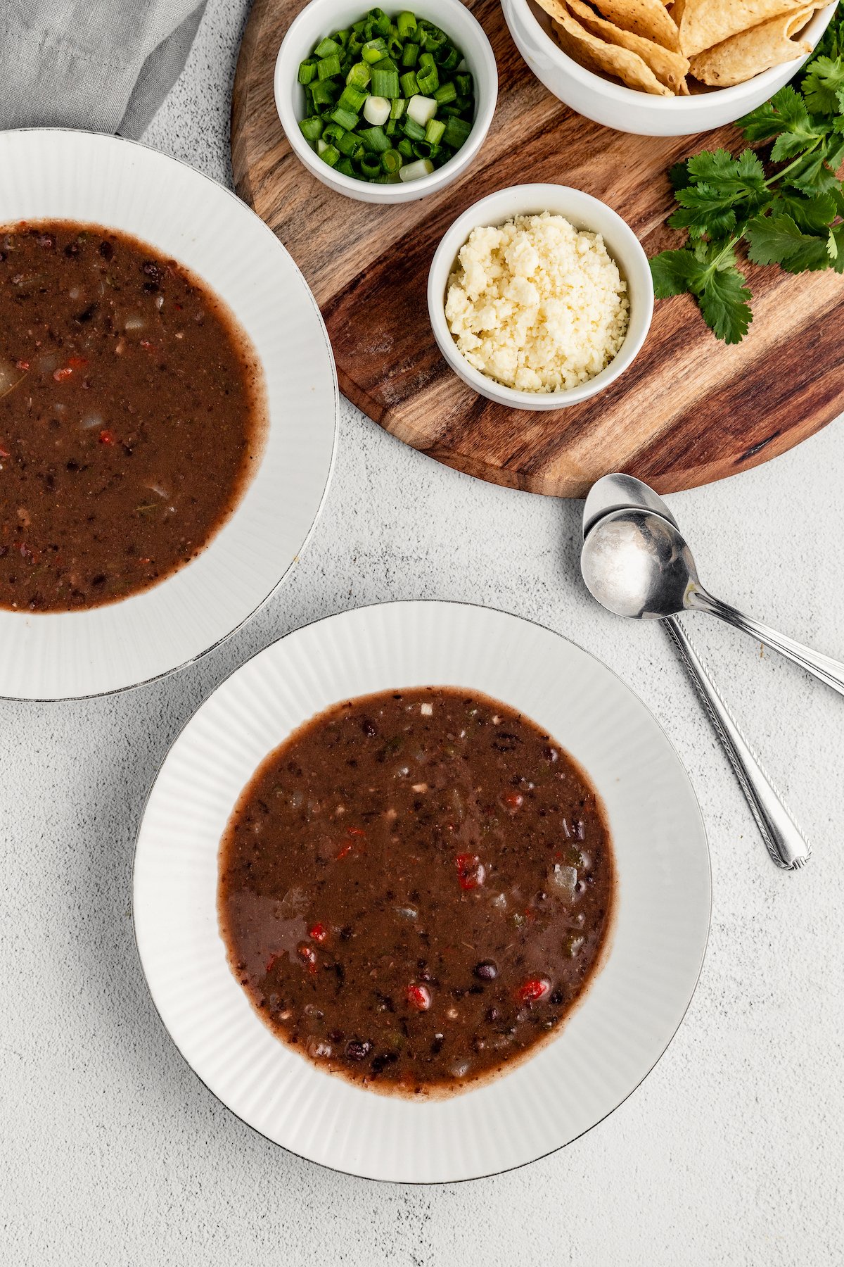 Black bean soup dished up into two bowls, next to a tray of toppings.