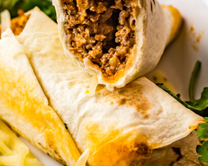 Two rolled tacos on a plate. One has been cut in half to show the texture of the filling.