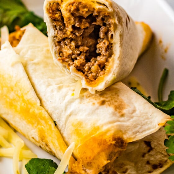 Two rolled tacos on a plate. One has been cut in half to show the texture of the filling.