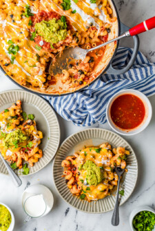 A chicken enchilada pasta bake in a round baking dish, with two servings on dinner plates nearby, along with a dish of salsa.