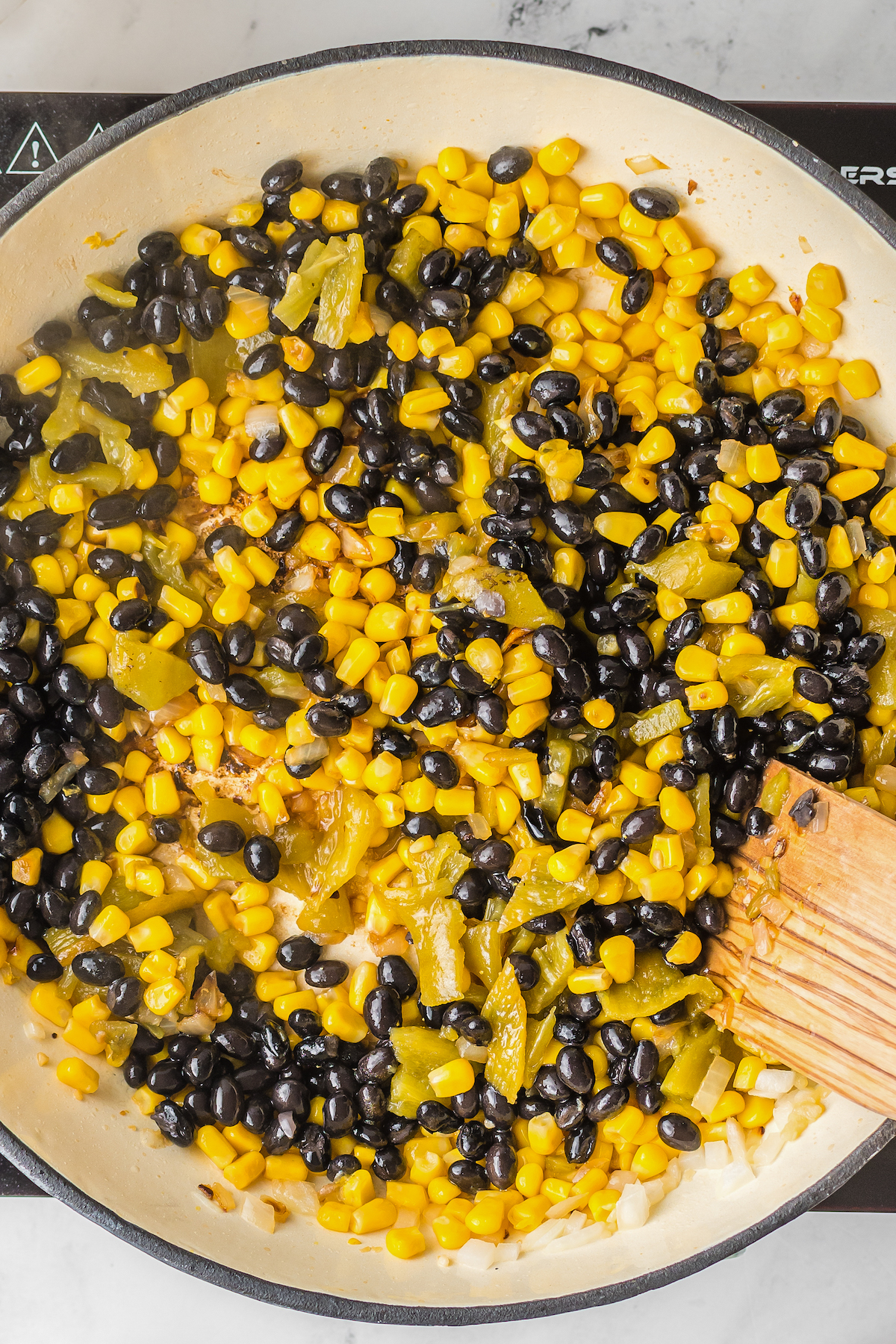 Corn, black beans, and other ingredients sauteing in a large skillet.